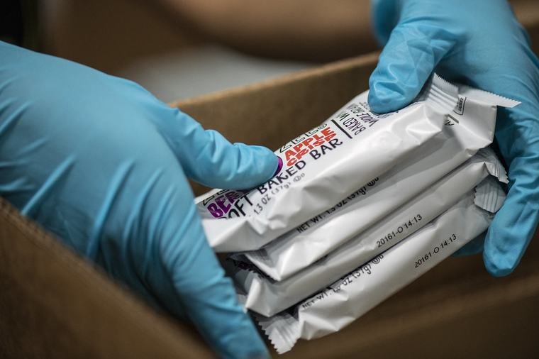 Gloved hands placing sealed units into a carton during prep